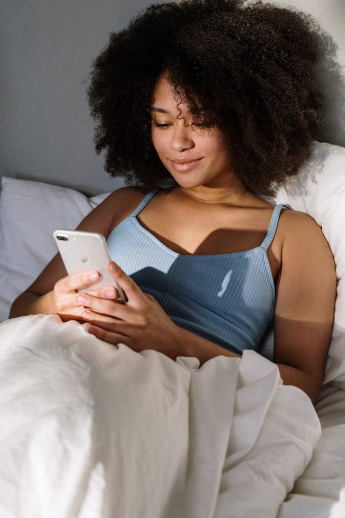 woman-apple-iphone-smartphone-4046303 African American woman enjoying a cozy morning in bed, using a smartphone.